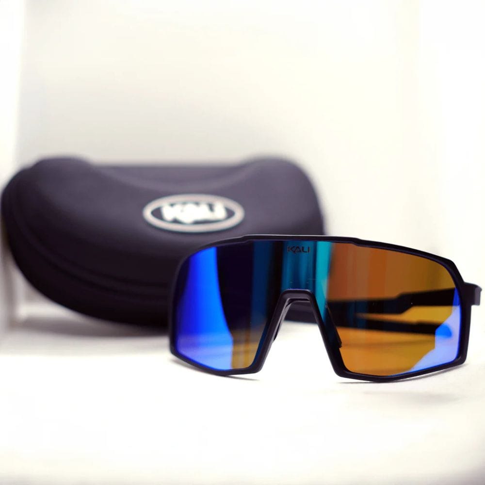 Sunglasses with blue and orange gradient lenses in front of a black case on a white background