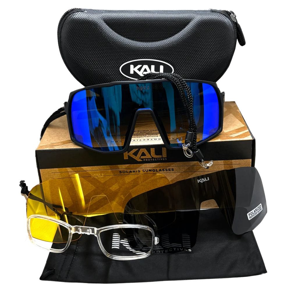 Kali sunglasses with blue and yellow lenses on a wooden block, surrounded by Kali branded cases and pouches.